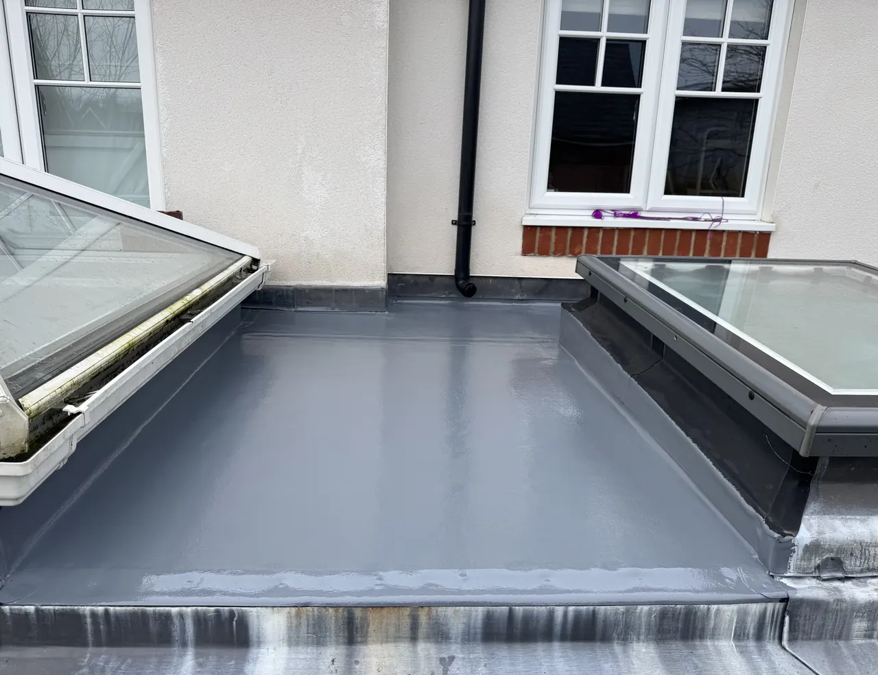 Grey fibreglass flat roof with a roof lantern and a flat skylight on a white rendered house