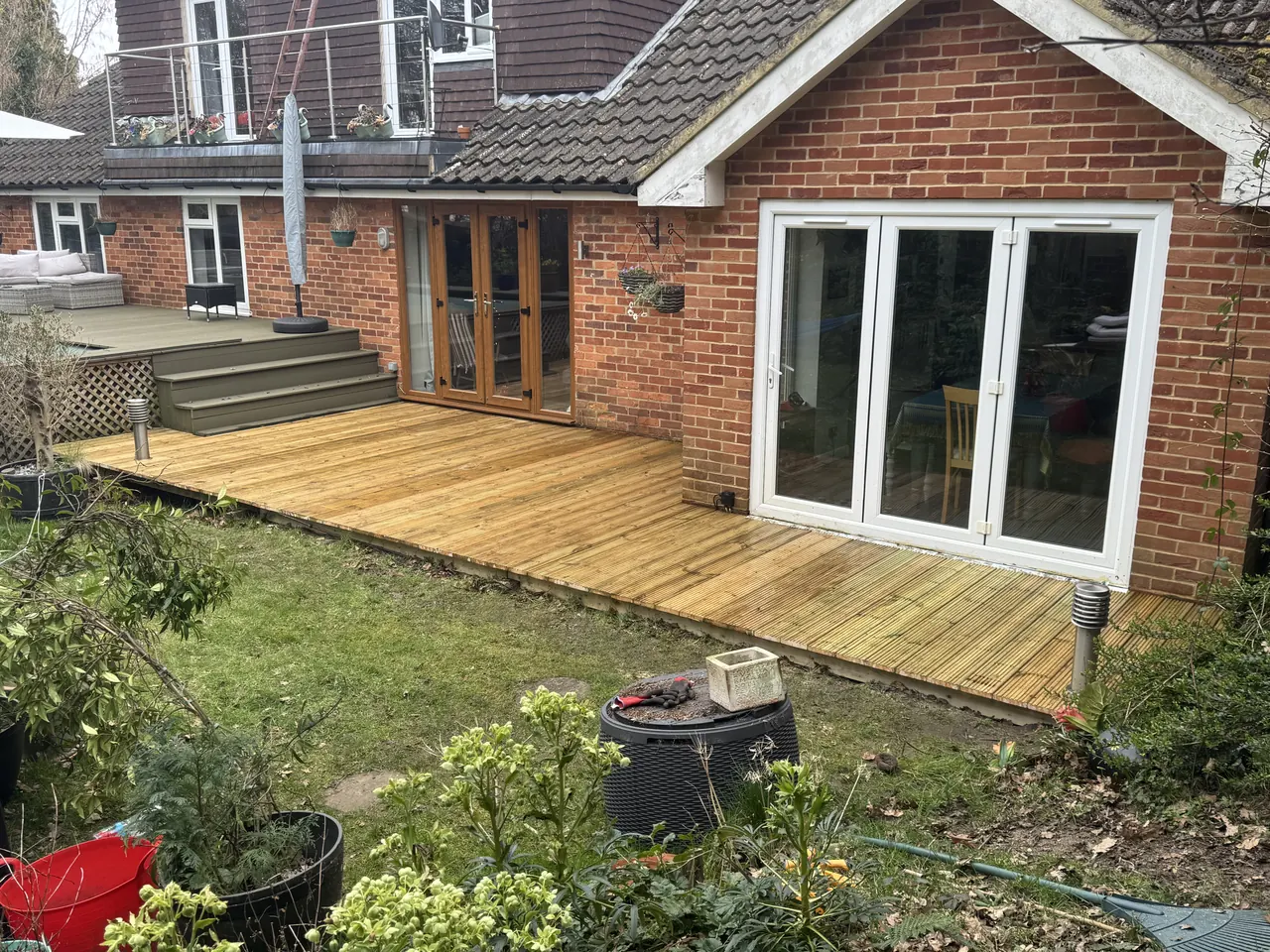 New softwood decking across the back of a brick house up to the bifold doors, with steps to the garden