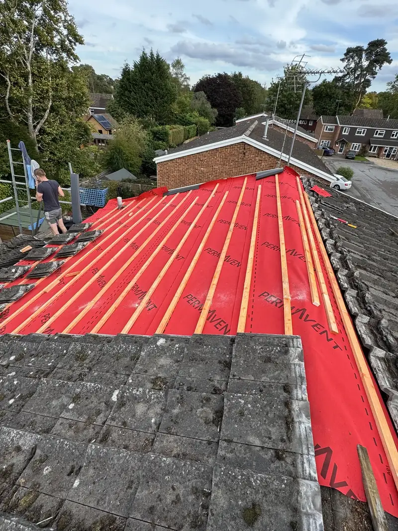 Red breathable membrane and battens over half a roof, roofer on the scaffold