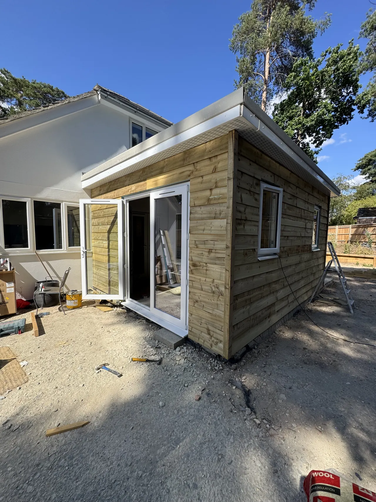 Timber-clad garden room with white bifold doors, fascia and soffit being fitted